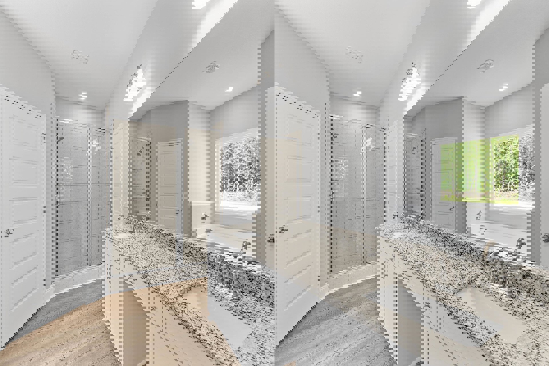 Bathroom featuring a marble countertop with undermount sink, glass-enclosed shower, white door with silver handle, window overlooking trees, and modern light fixture on the ceiling