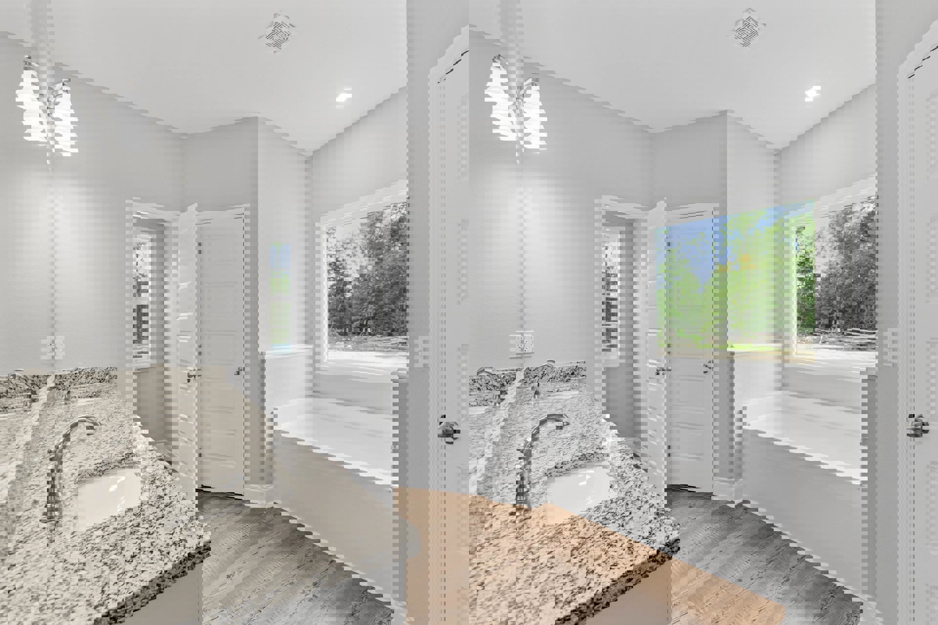 Bathroom featuring a white and black marble countertop, built-in bathtub, silver faucet fixtures, white door with silver knobs, window overlooking trees, and modern light fixture.