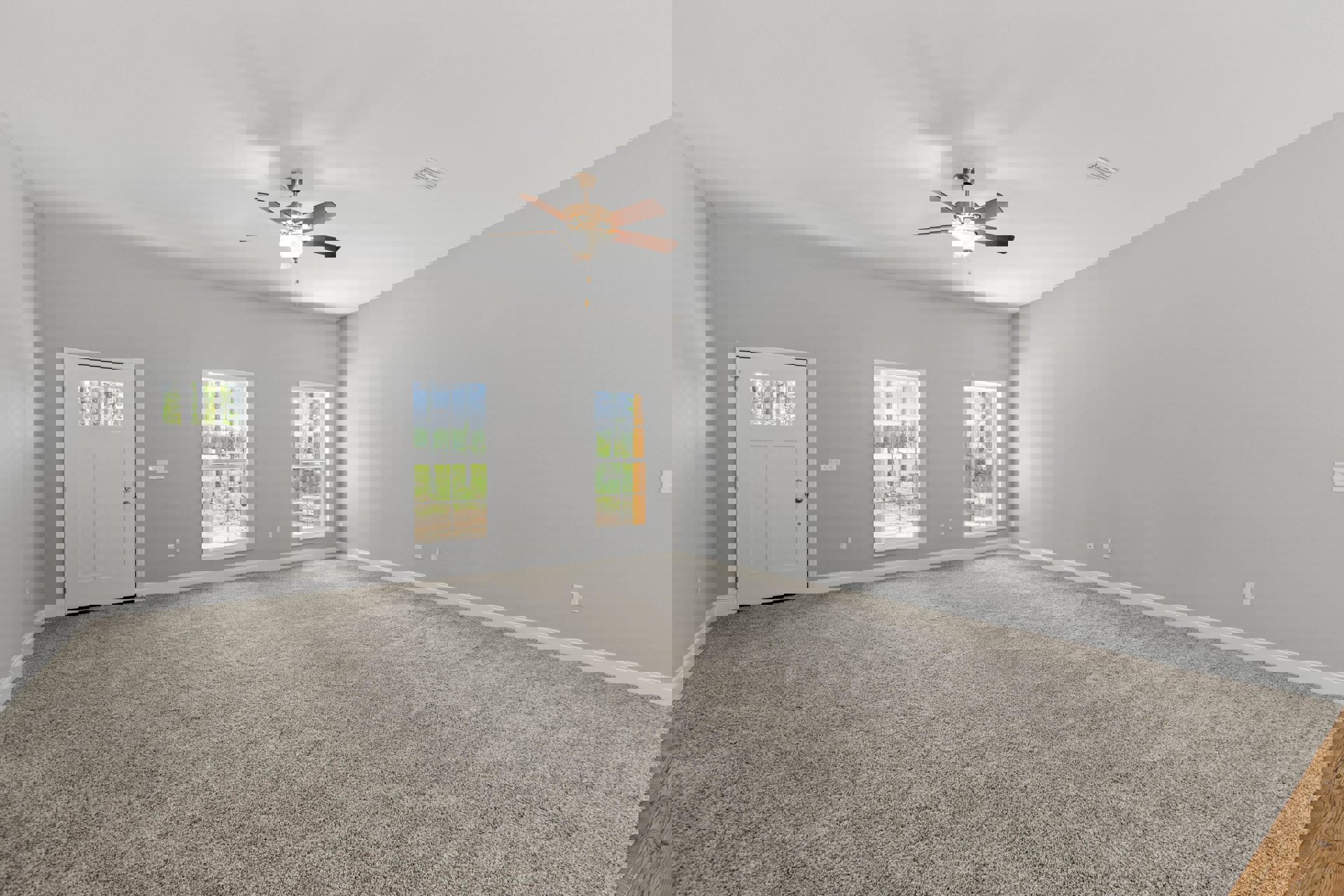 Carpeted room with ceiling fan, multiple windows showing trees and grass, white door with glass insert, light-colored walls and plaster ceiling