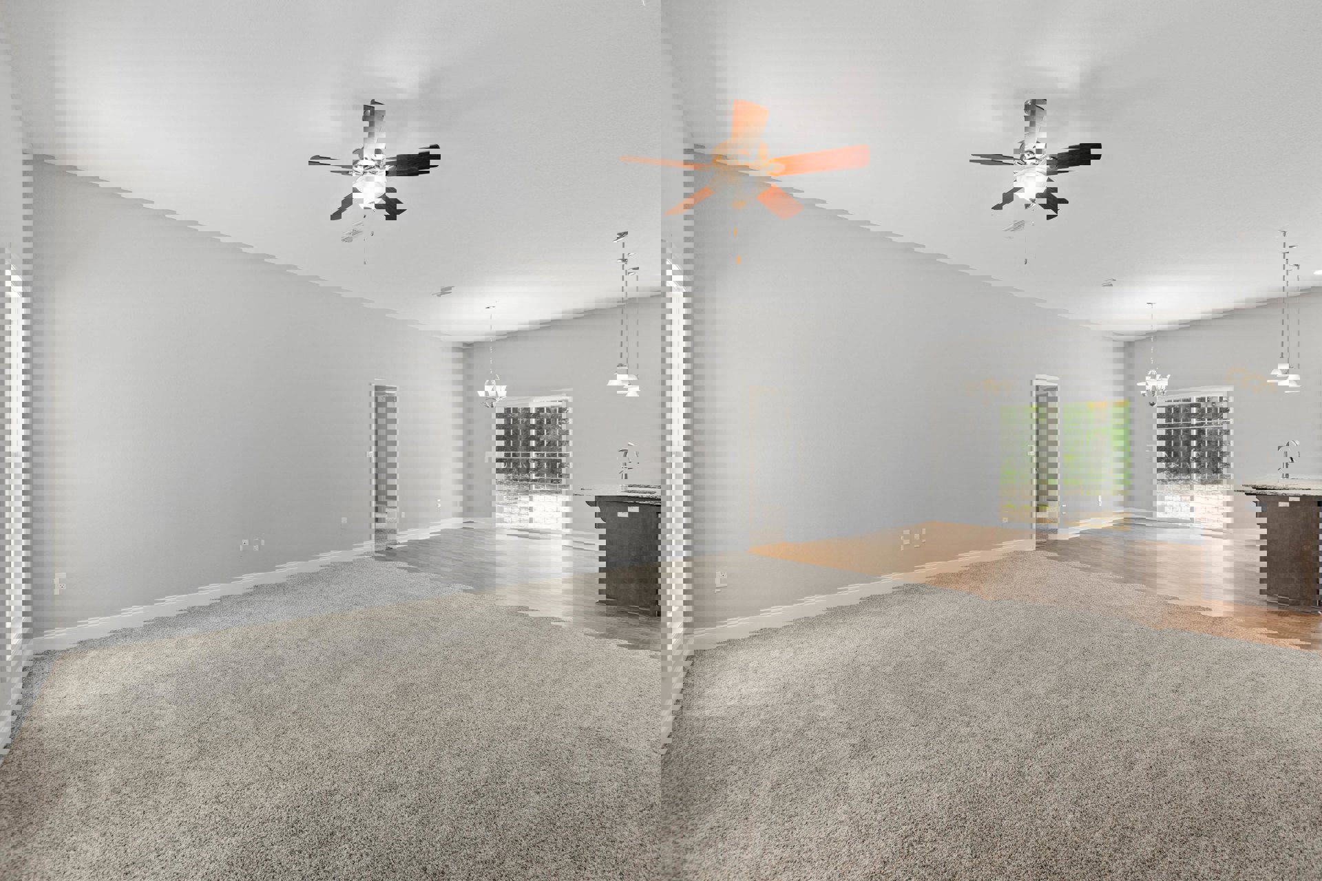 Carpeted living space with ceiling fan and light fixture, white door, sliding glass door overlooking trees, and kitchen island with marble countertop