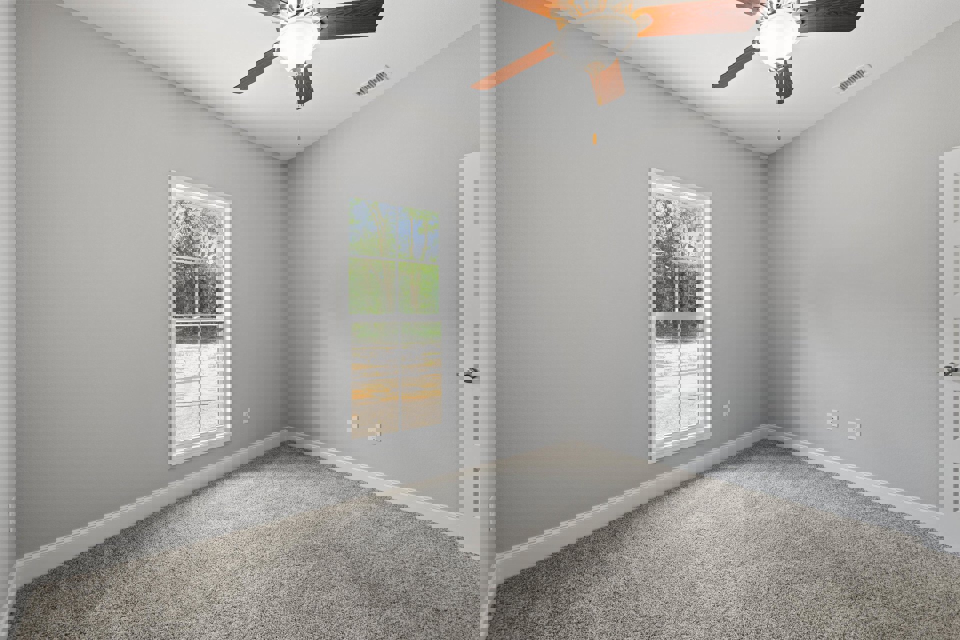 Carpeted room with white walls, central ceiling fan with light fixture, large window overlooking trees, black wall-mounted object.