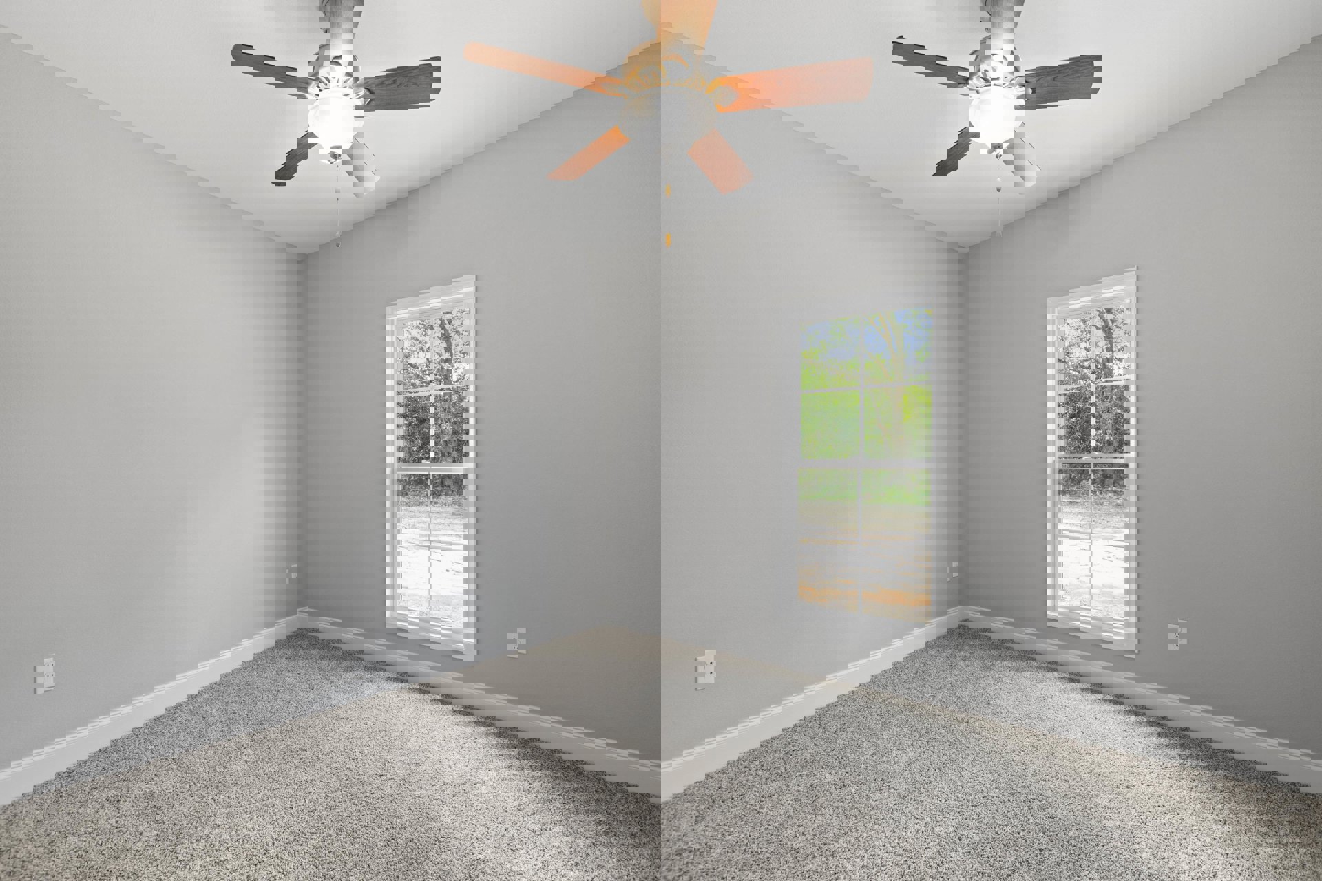 Ceiling fan with integrated light fixture mounted on white plaster ceiling, carpeted floor, large window revealing leafy trees outside