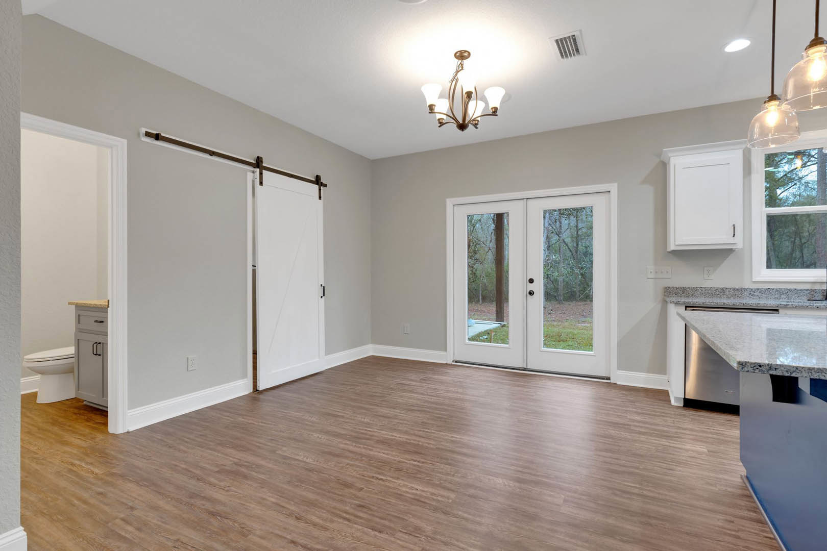Wood flooring in a kitchen with white cabinetry featuring black handles, glass-paneled double sliding doors, five-light ceiling fixture, and adjacent bathroom with closed toilet