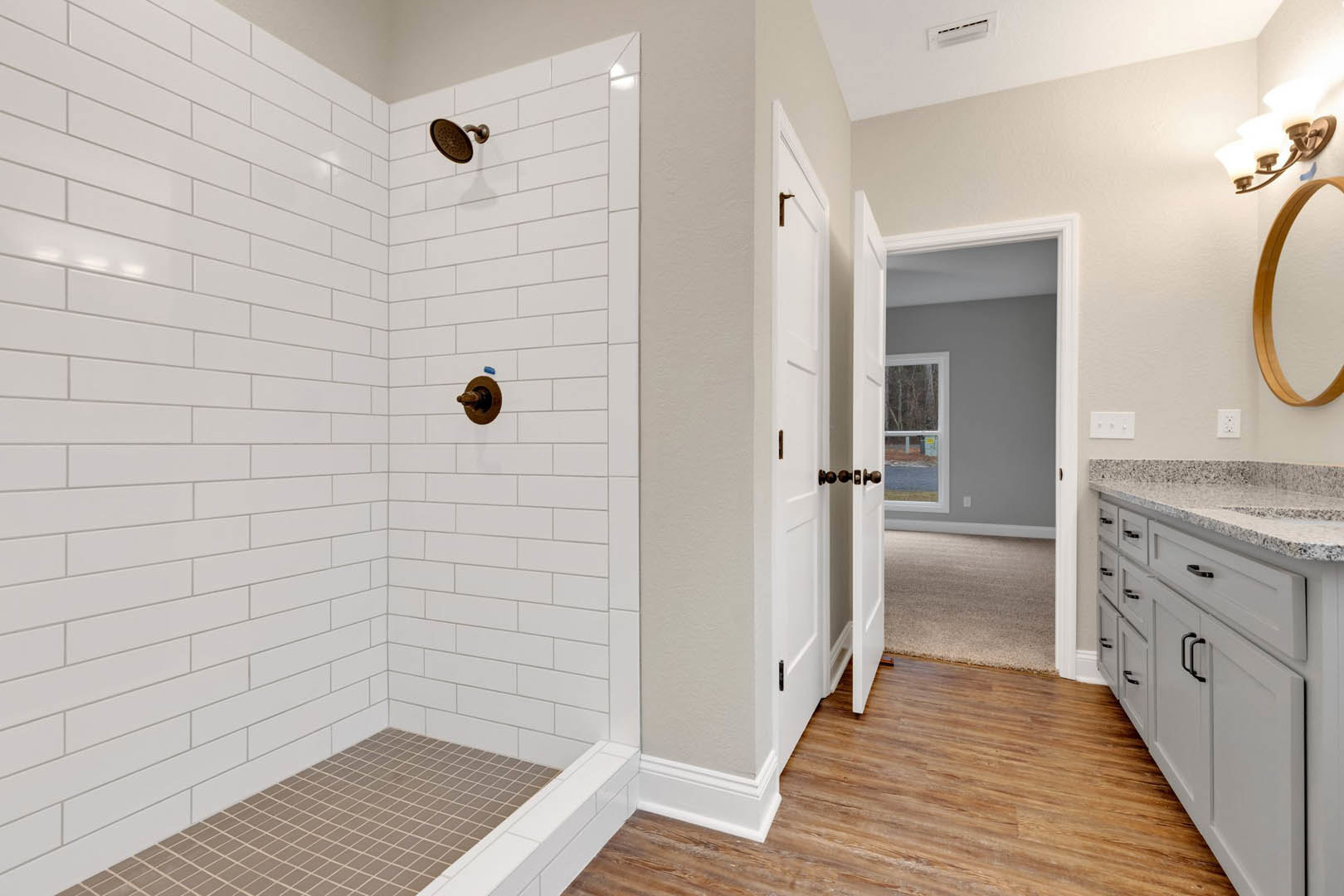 Bathroom with brown tile floor, white tile accents, glass shower enclosure, wall-mounted shower head, white sink with chrome faucet, wooden chair near vanity, and modern cabinetry.