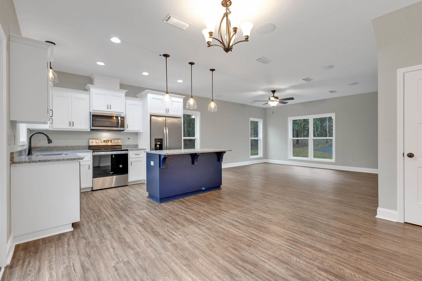 Open kitchen and living room featuring wood flooring, blue island with marble countertop, open oven door, microwave with illuminated interior, cabinetry, and window overlooking