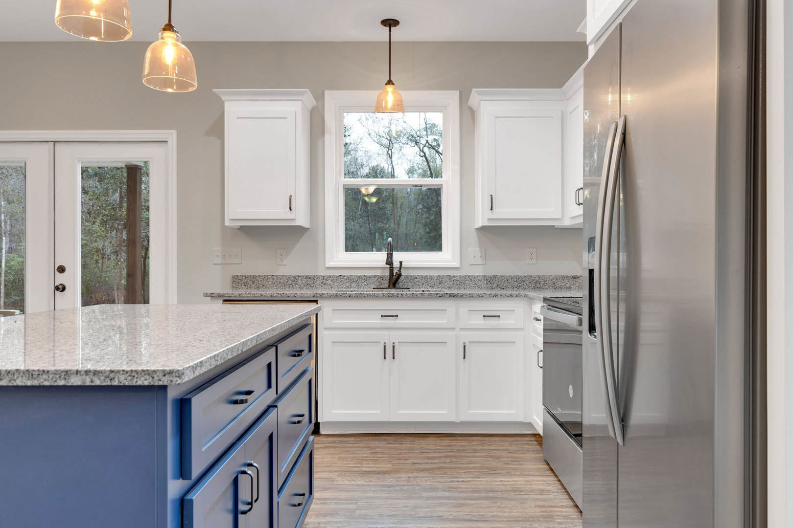 White kitchen cabinets and blue island with wood countertop, tile backsplash, stainless sink, drawers, and window showing trees outside