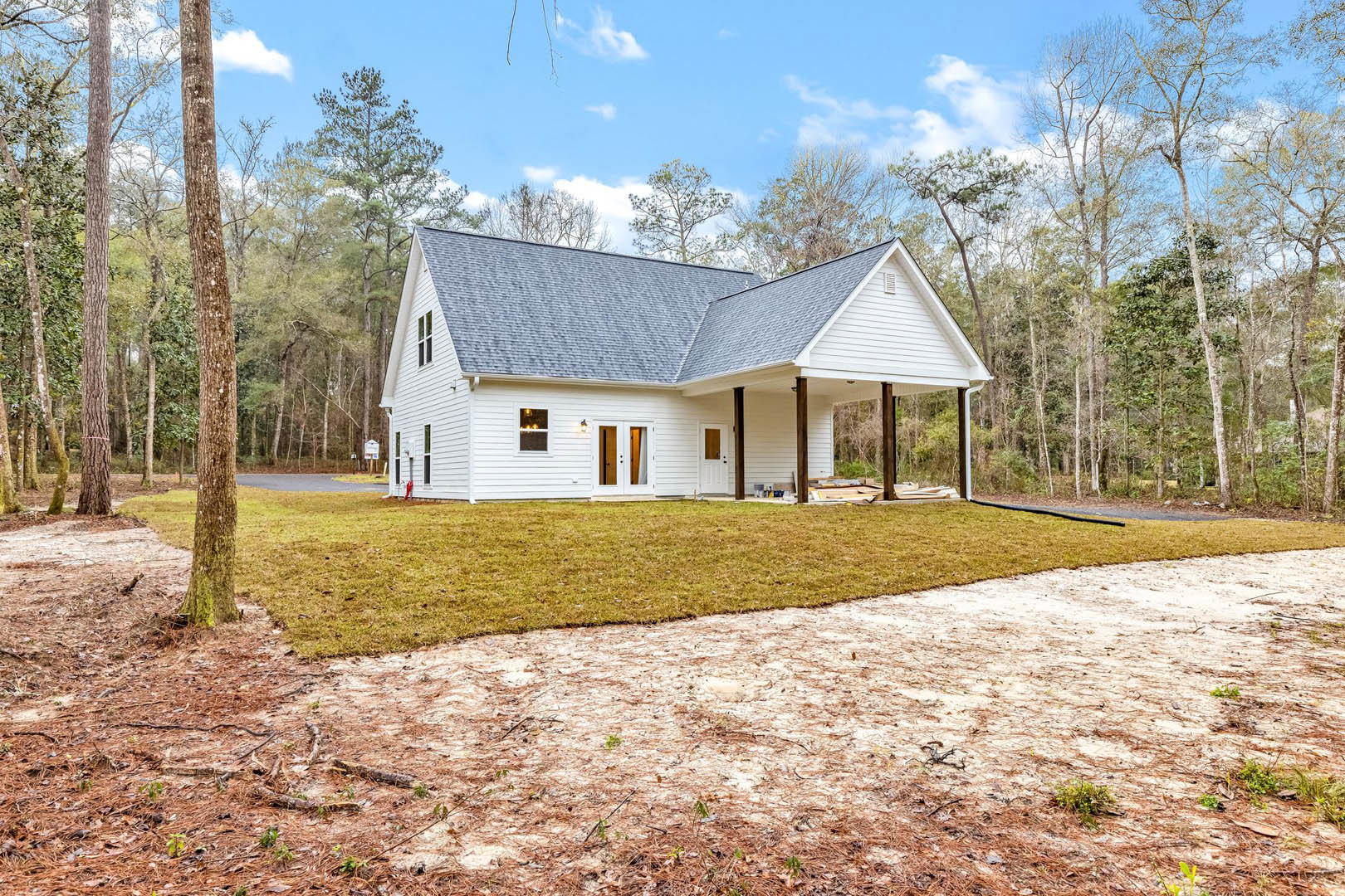 White farmhouse with covered porch, surrounded by green lawn and mature trees under a partly cloudy sky