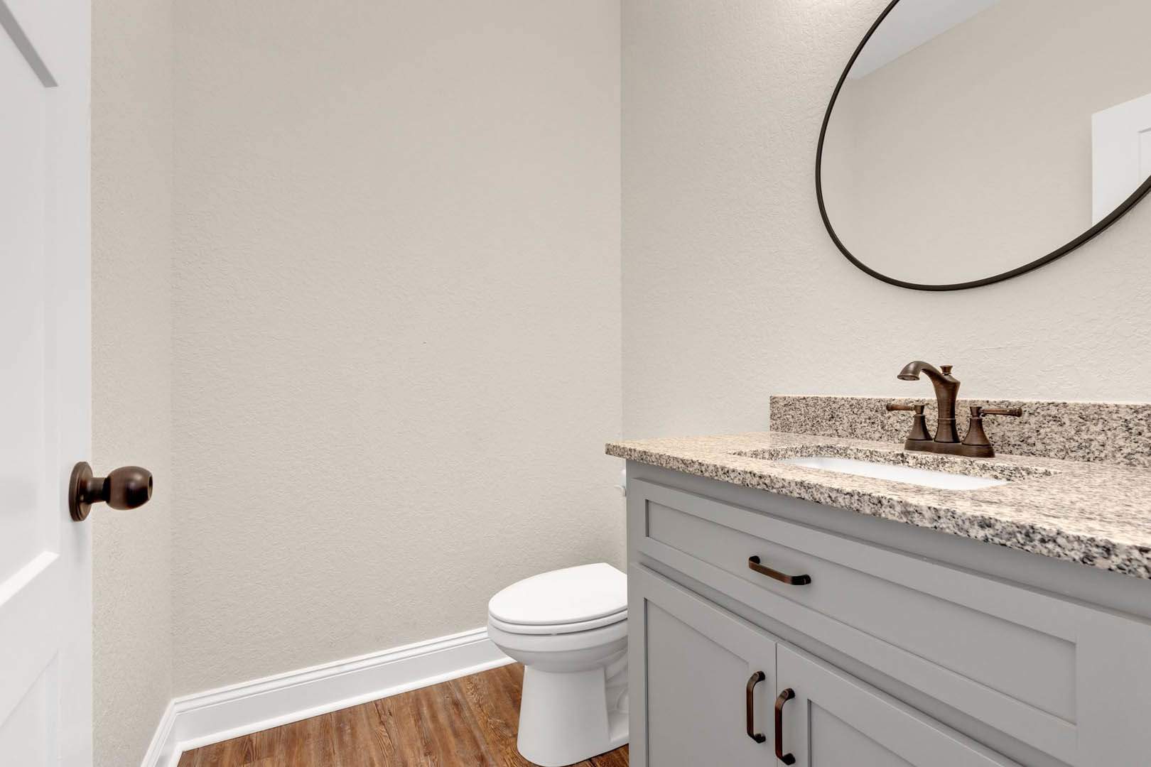 White bathroom with round wall mirror above rectangular sink, chrome faucet, tiled backsplash, and light wood cabinetry with drawers