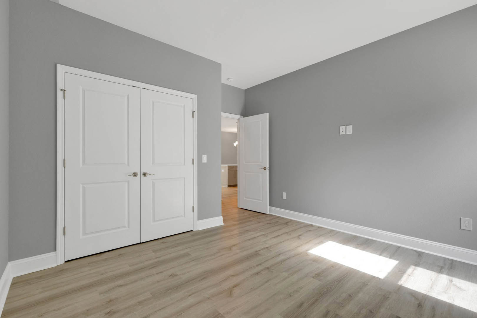 Hardwood floor room with double white doors, white walls, and brushed metal door handles