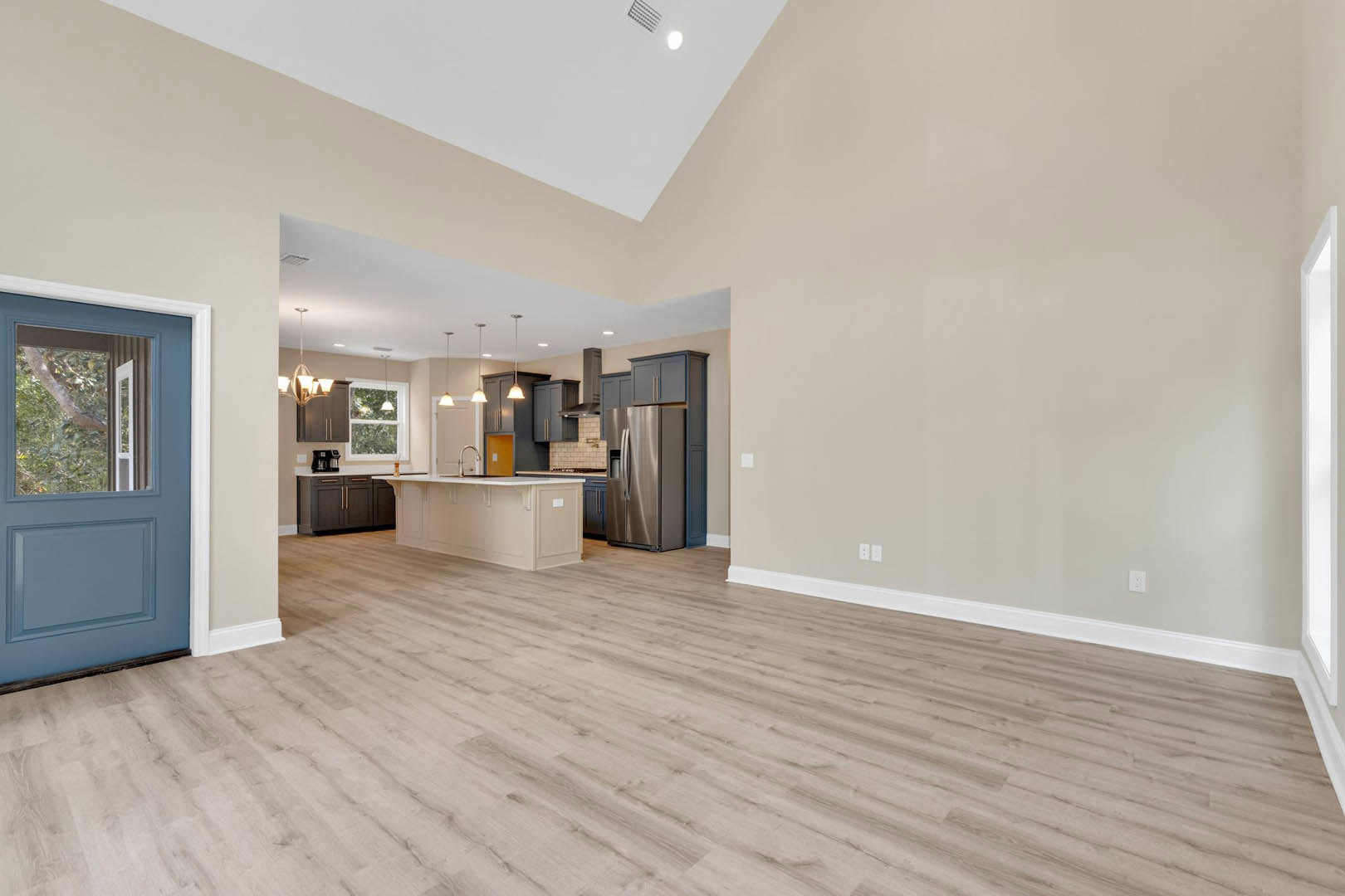 Spacious open floor plan featuring a kitchen with white countertops, stainless steel refrigerator, hardwood flooring, blue door with window, and adjacent white door and window