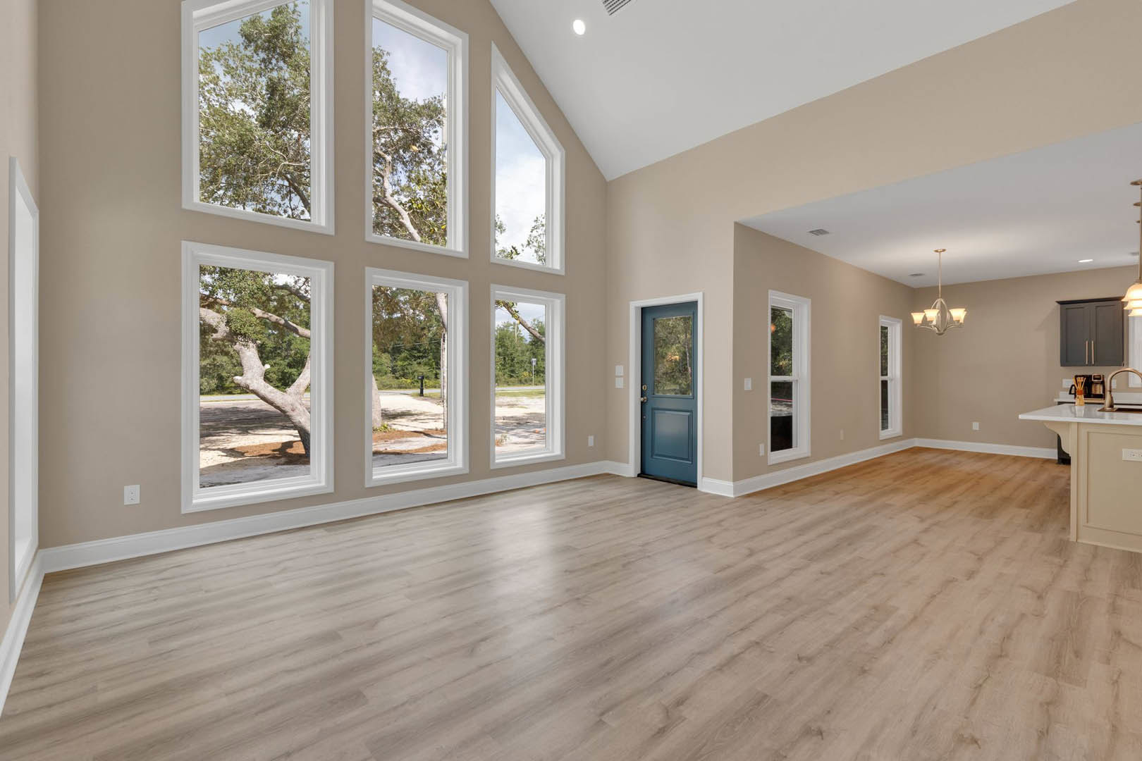 Spacious room featuring a wall of tall windows overlooking trees, blue door with glass panels, light wood flooring, ceiling light fixture, and natural light illuminating the