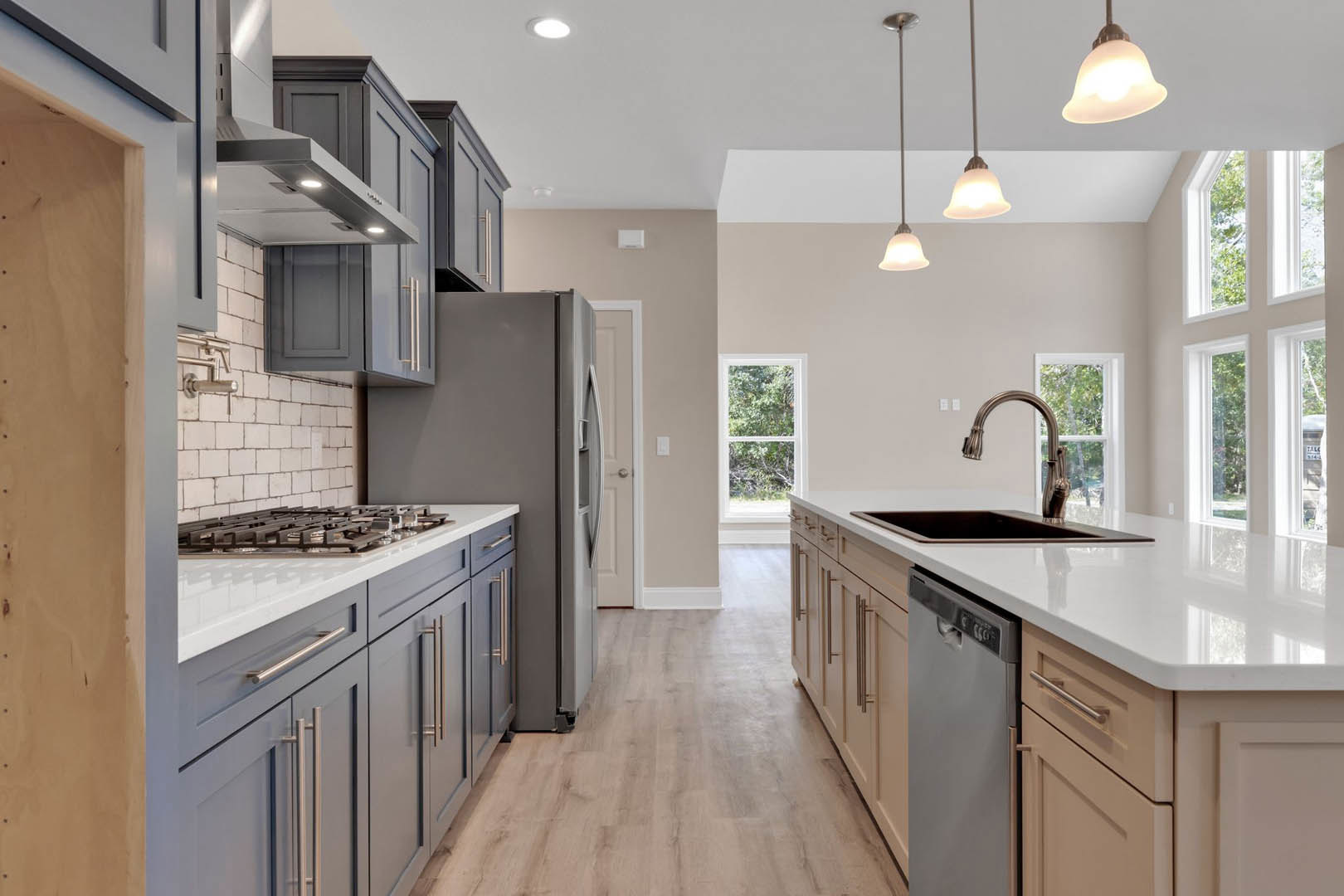 Kitchen with stainless steel refrigerator, stove, white-framed window, light fixture, metal faucet, black rectangular object on white countertop, and white cabinetry with drawers