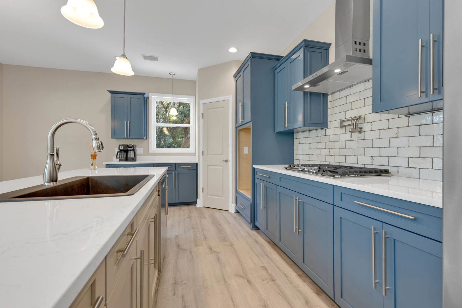 Blue kitchen cabinets with white countertops, silver faucet and sink, white door with silver handle, window with white frame, white light fixture, close-up shelf detail, tiled