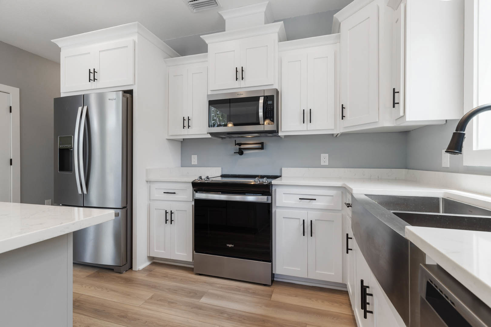White shaker cabinets, stainless steel appliances including a black and silver oven, open microwave door, close-up refrigerator, chrome faucet, wood flooring, and stone countertops