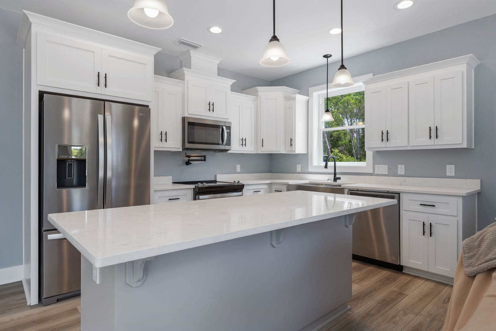 White kitchen cabinets, quartz countertop, stainless steel refrigerator with ice maker, built-in microwave, modern ceiling light fixture, undermount sink, neutral walls