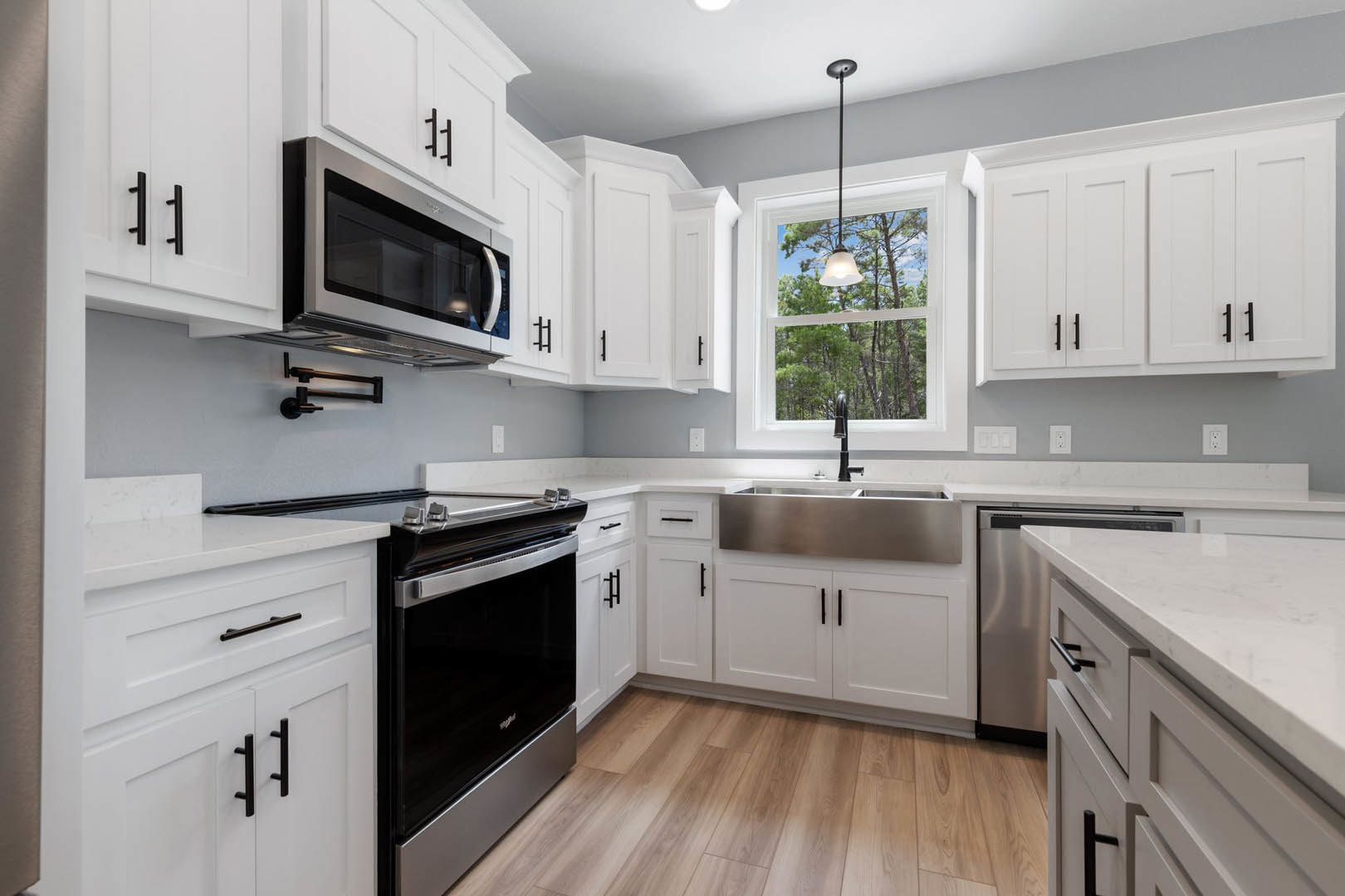 White kitchen cabinets, stainless steel appliances, wood flooring, black and silver oven, built-in microwave with overhead lighting, window light, close-up of sink and countertop.