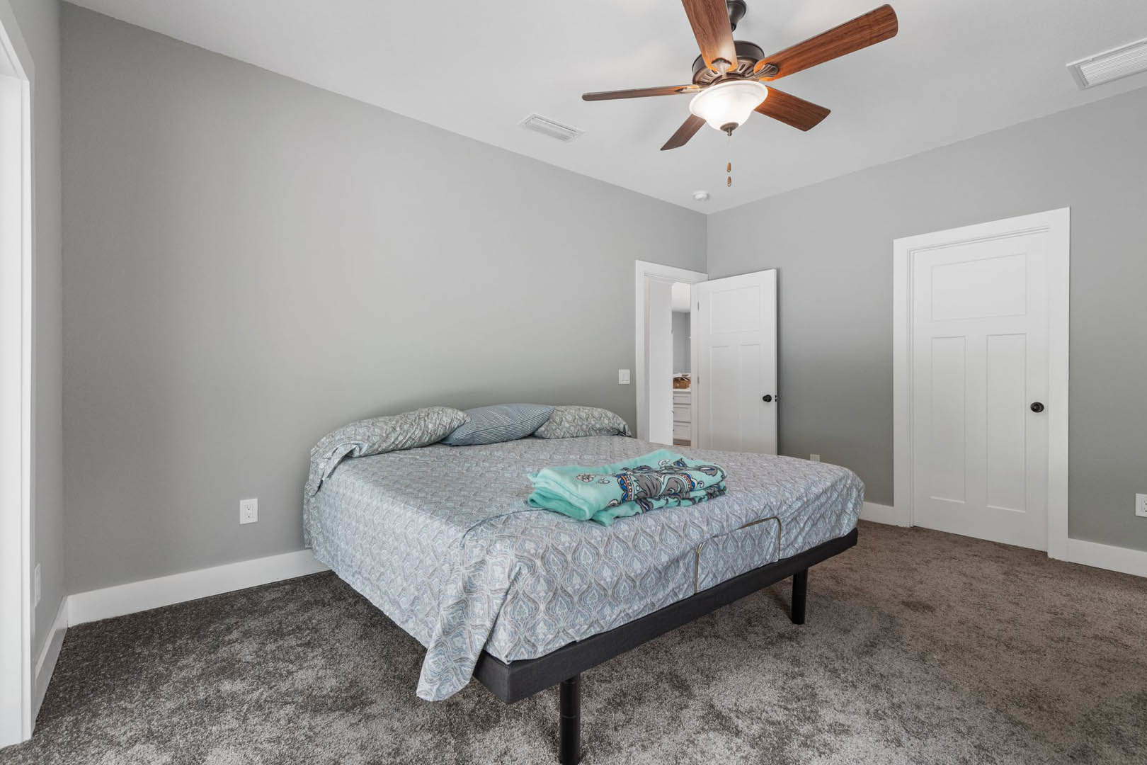Queen bed with cartoon blanket and pillow, dark wood frame, ceiling fan with light fixture above, white door with black handle, neutral walls and flooring