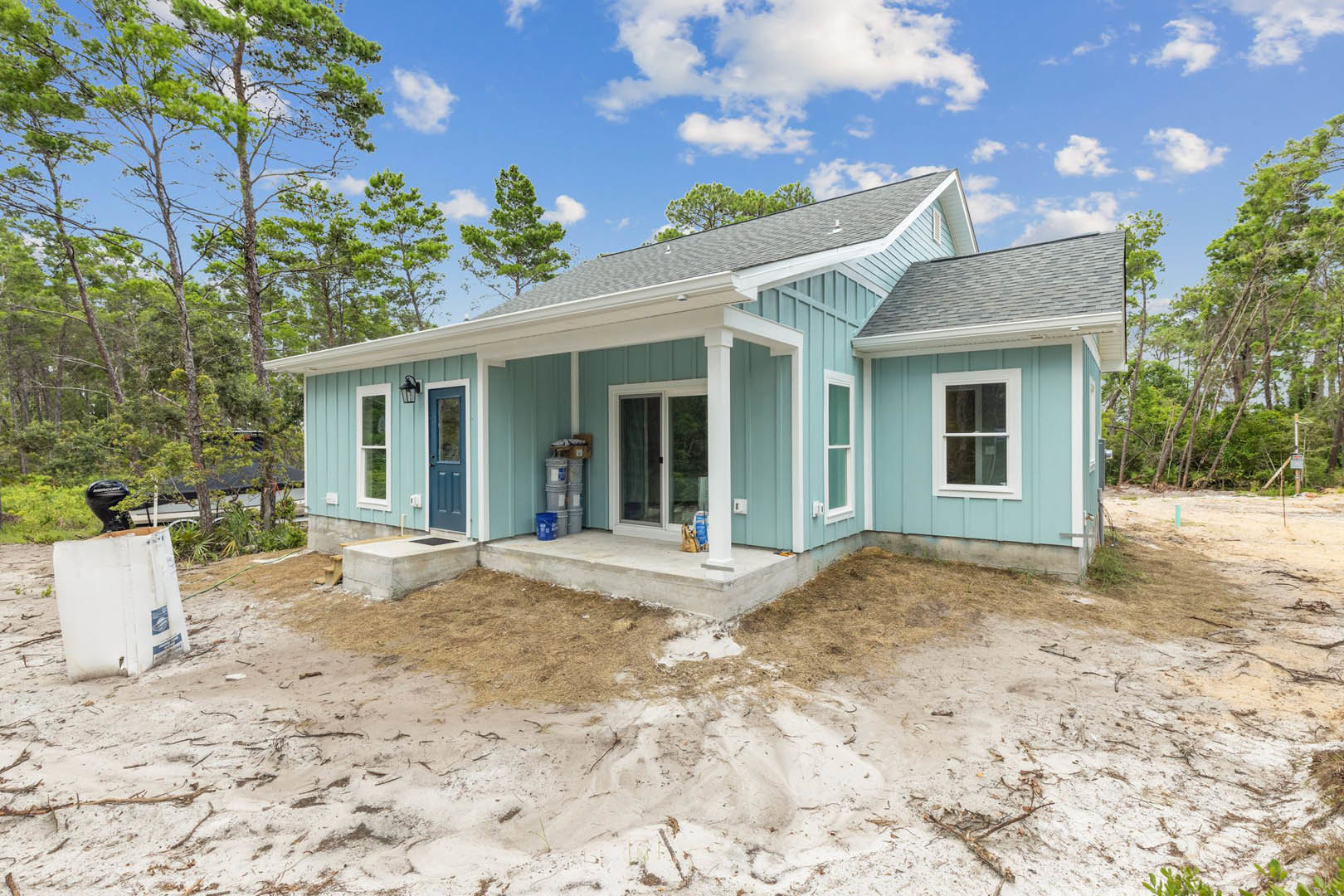 Modern home exterior with white siding, covered porch, white-framed windows, and a dirt area in the front yard; small white utility box sits on the ground near a pile of soil.