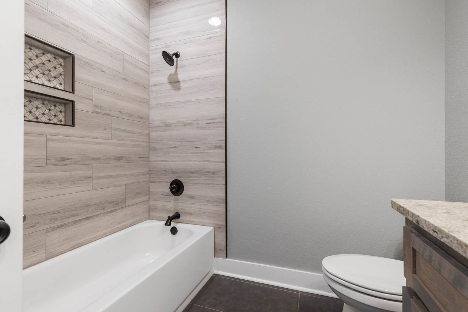 White freestanding bathtub and modern toilet on light wood flooring, black faucet and shower head, white tile walls
