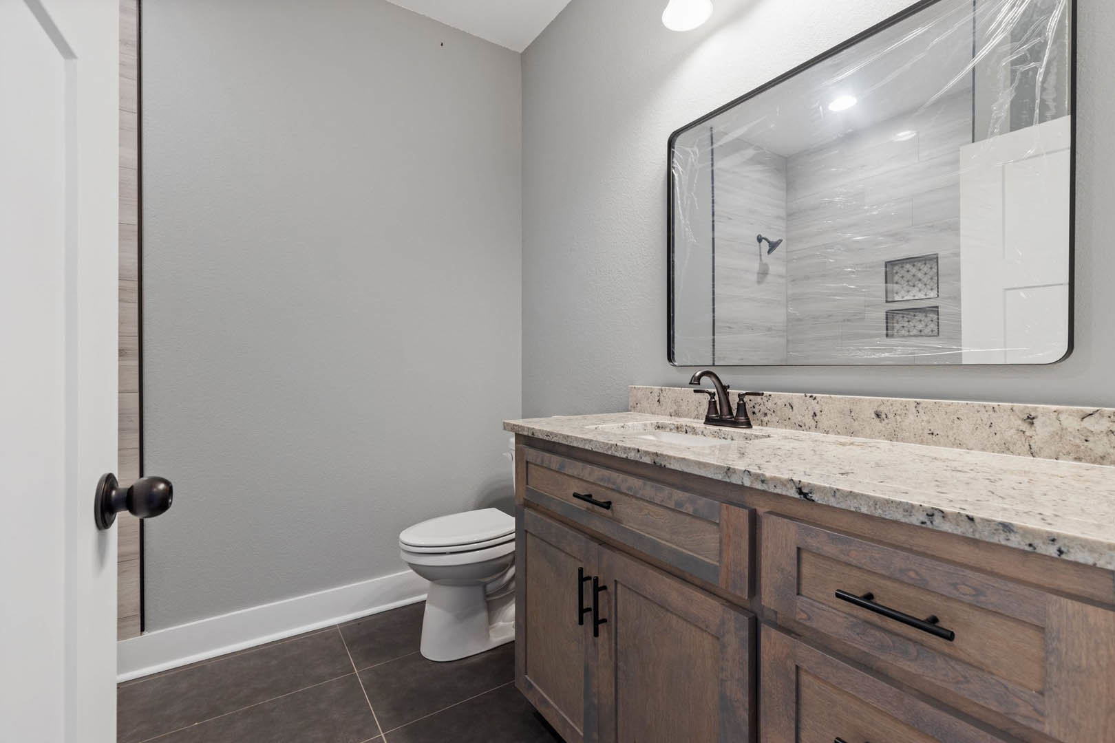 White bathroom with rectangular mirror above a modern sink, chrome faucet, tiled walls, and wood cabinetry with black handle