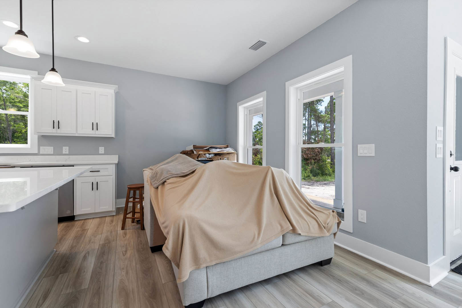 Bedroom with wood flooring, bed with white linens, blanket draped over nearby couch, wooden ladder leaning against white wall, rectangular wall decor with three square cutouts