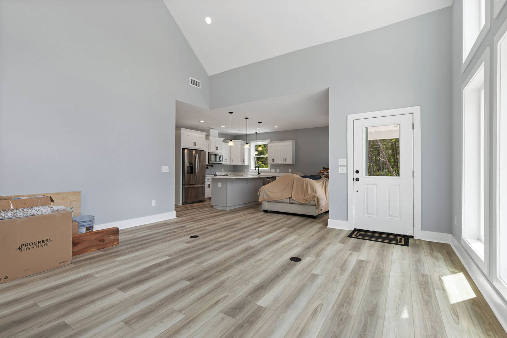 Living room with wood flooring, white door featuring glass window, couch draped with a blanket, refrigerator and cabinetry, window overlooking trees