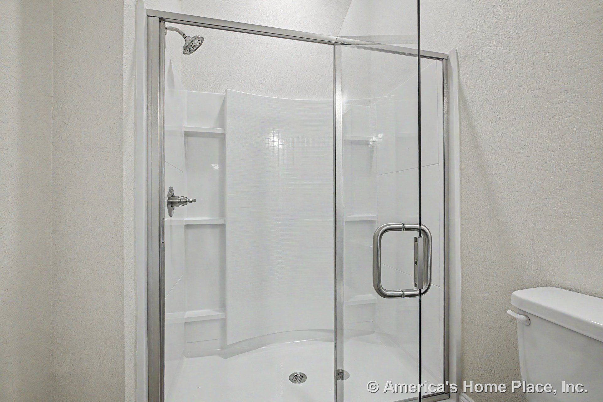 Frameless glass walk-in shower with chrome showerhead, white tile walls, built-in shower shelves, curved shower base, and adjacent toilet.
