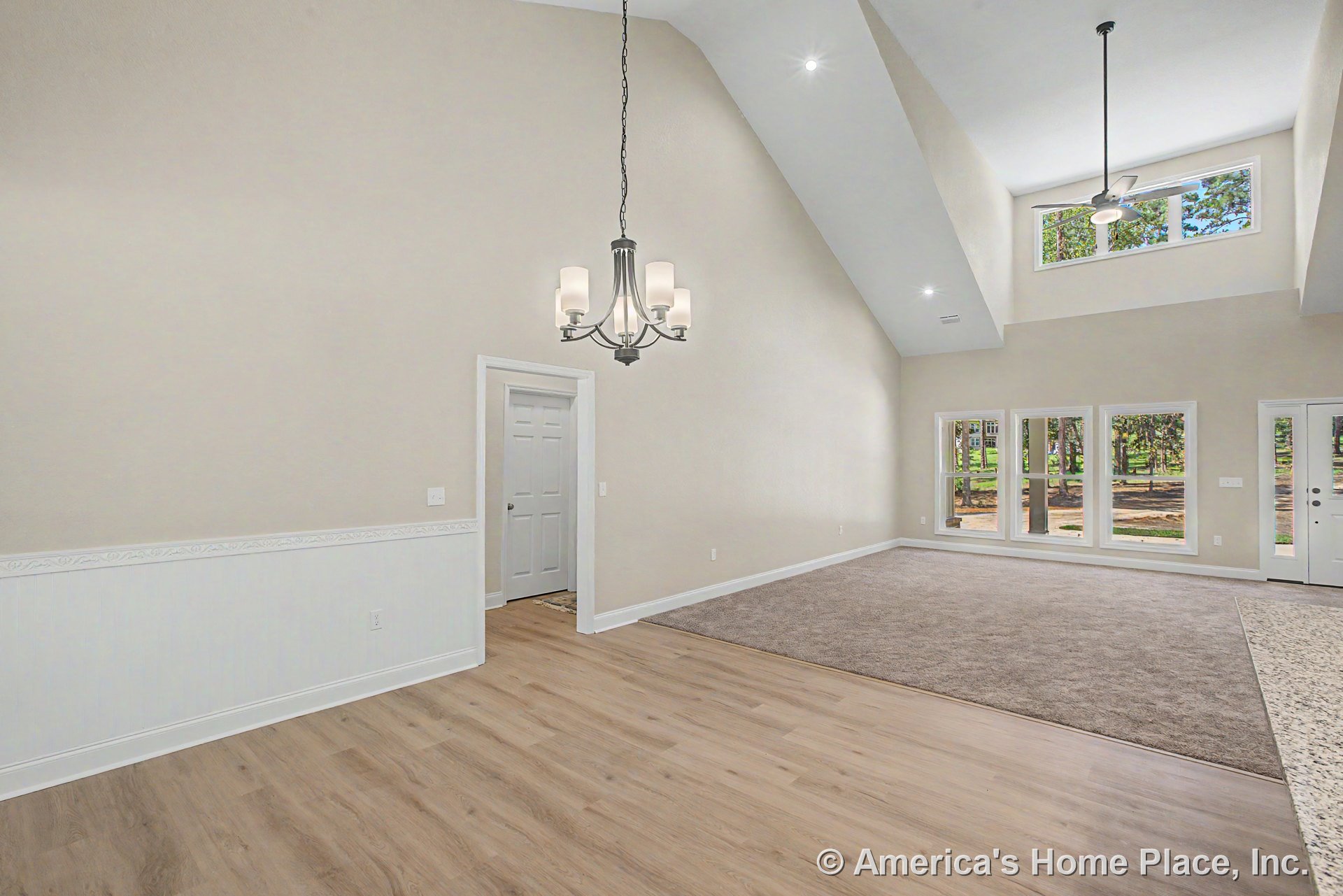 Vaulted ceiling living room with expansive window wall, carpeted seating area, wood-look flooring, modern chandelier, white trim and wainscoting, interior door, recessed lighting
