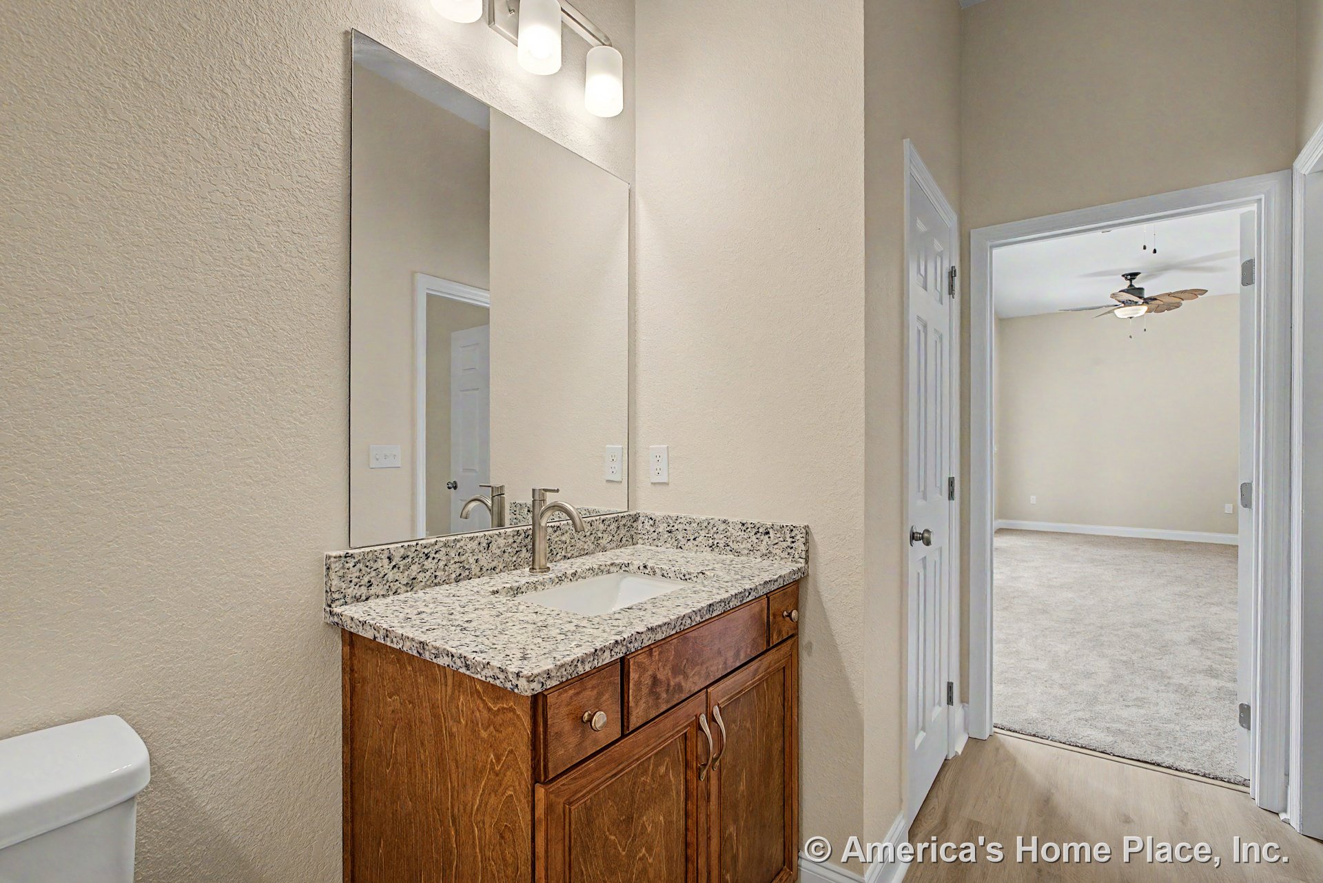 Granite vanity with undermount sink, wood cabinetry, large wall mirror, built-in overhead lighting, neutral painted walls, white trim, and hard surface flooring.