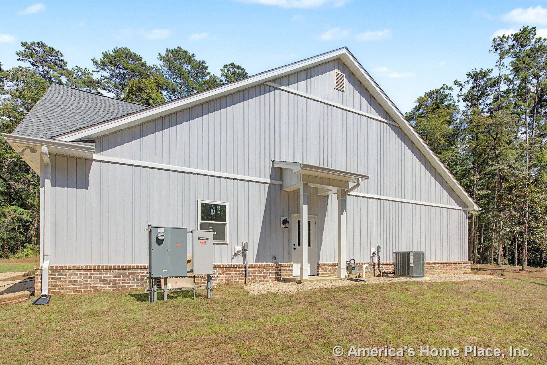Vertical siding exterior with brick foundation trim, covered entry porch featuring a single door, utility boxes mounted near the side yard, asphalt shingle gabled roof, window