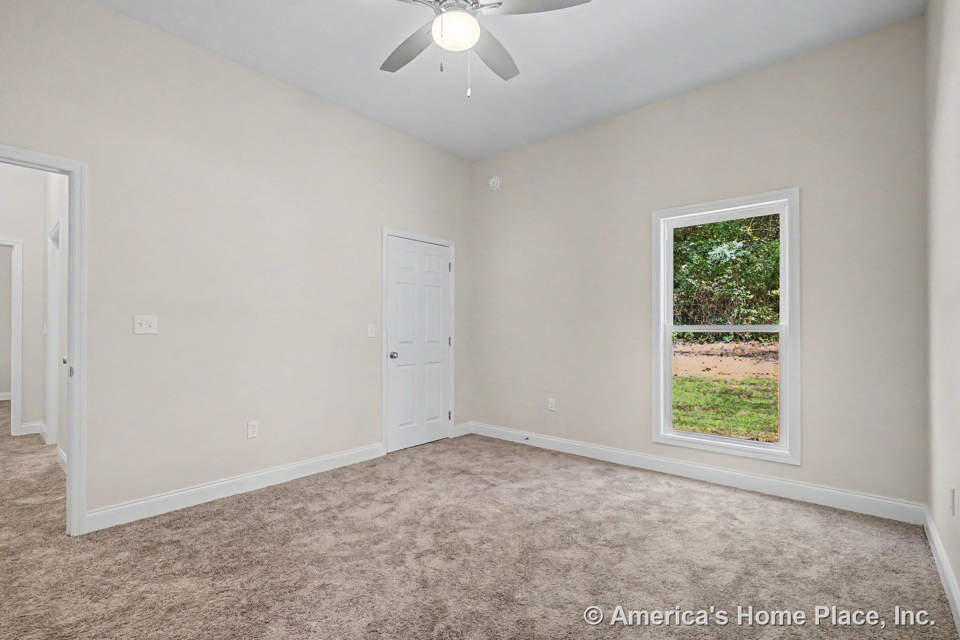 Bedroom with large single window framed in white trim, neutral carpet flooring, light beige walls, white baseboards, white interior door, and ceiling fan with integrated light