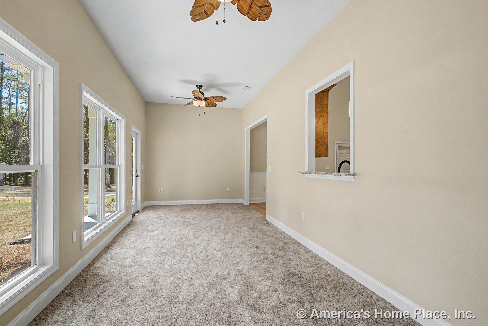 Sunroom with expansive windows, beige carpet flooring, leaf-shaped ceiling fans, white trim, pass-through window featuring a granite ledge, neutral wall color, high ceiling, and