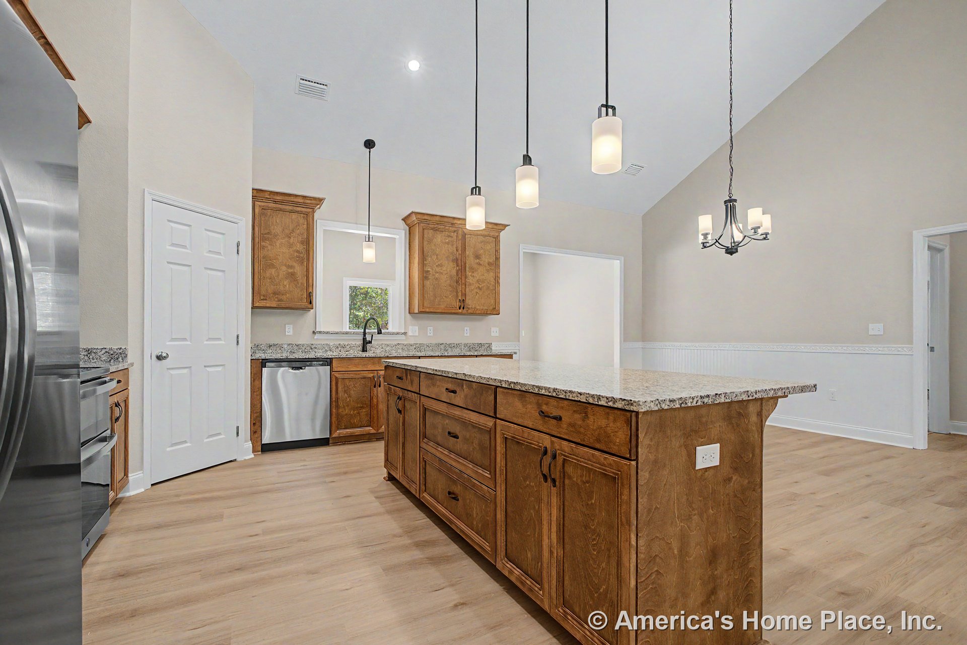 Custom kitchen with wood cabinetry, granite countertops, central island, stainless steel appliances, pendant lighting, vaulted ceiling, light wood flooring, and decorative trim.