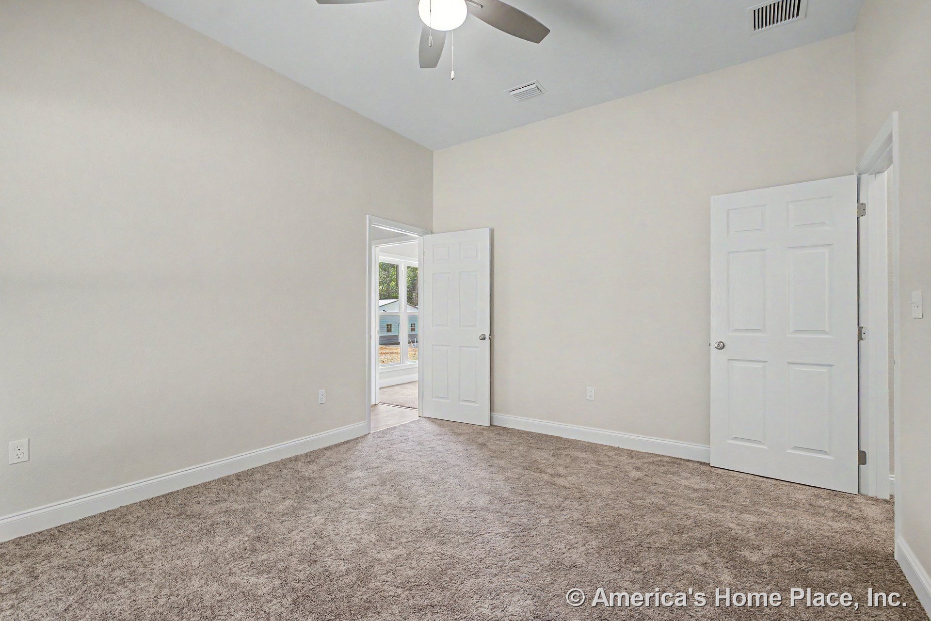 Bedroom with neutral carpet flooring, white baseboards, paneled white doors, light beige walls, ceiling fan with integrated light, vented ceiling, and door hardware.