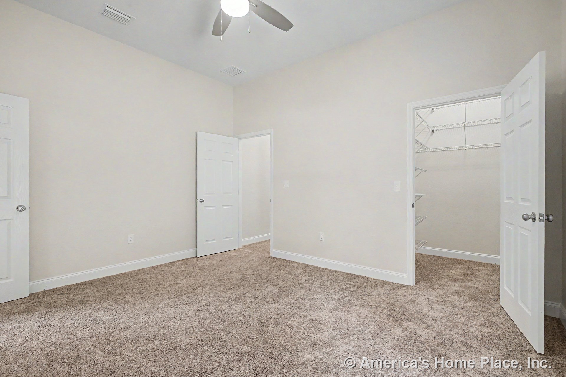 Carpeted bedroom with white baseboards, neutral walls, ceiling fan with light, three-panel white doors, and walk-in closet featuring wire shelving.