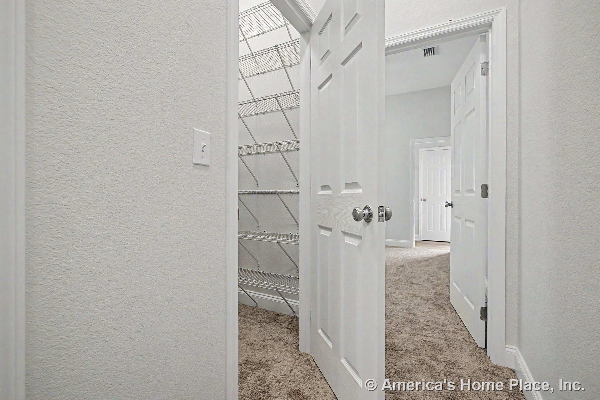 Hallway with carpet flooring, white paneled doors, closet featuring wire shelving, textured wall finish, baseboard trim, ceiling vent, and visible door hardware and light switch.
