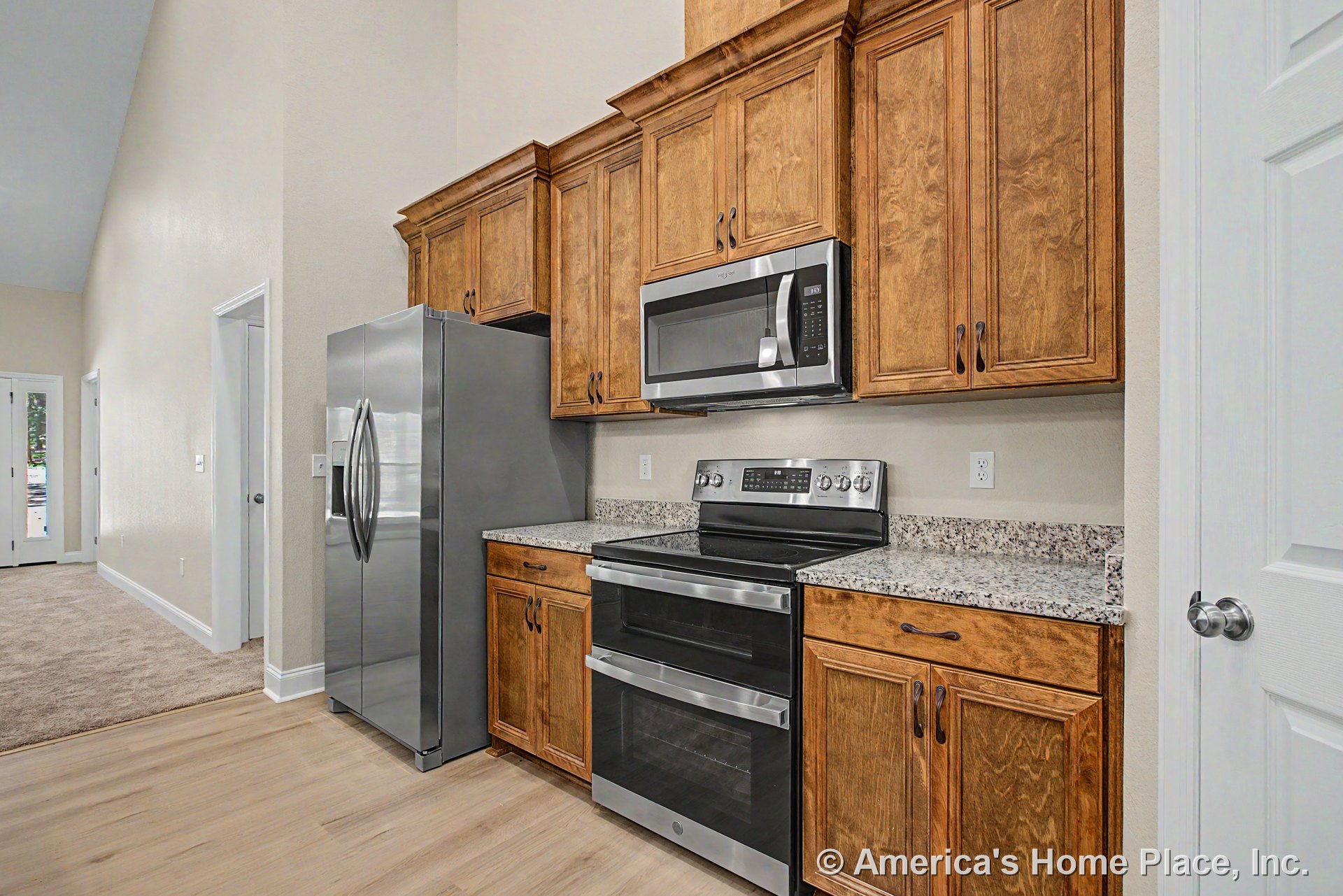 Custom kitchen with upper and lower wood cabinetry, granite countertops, stainless steel refrigerator, oven, and microwave, light wood flooring, and neutral wall paint.