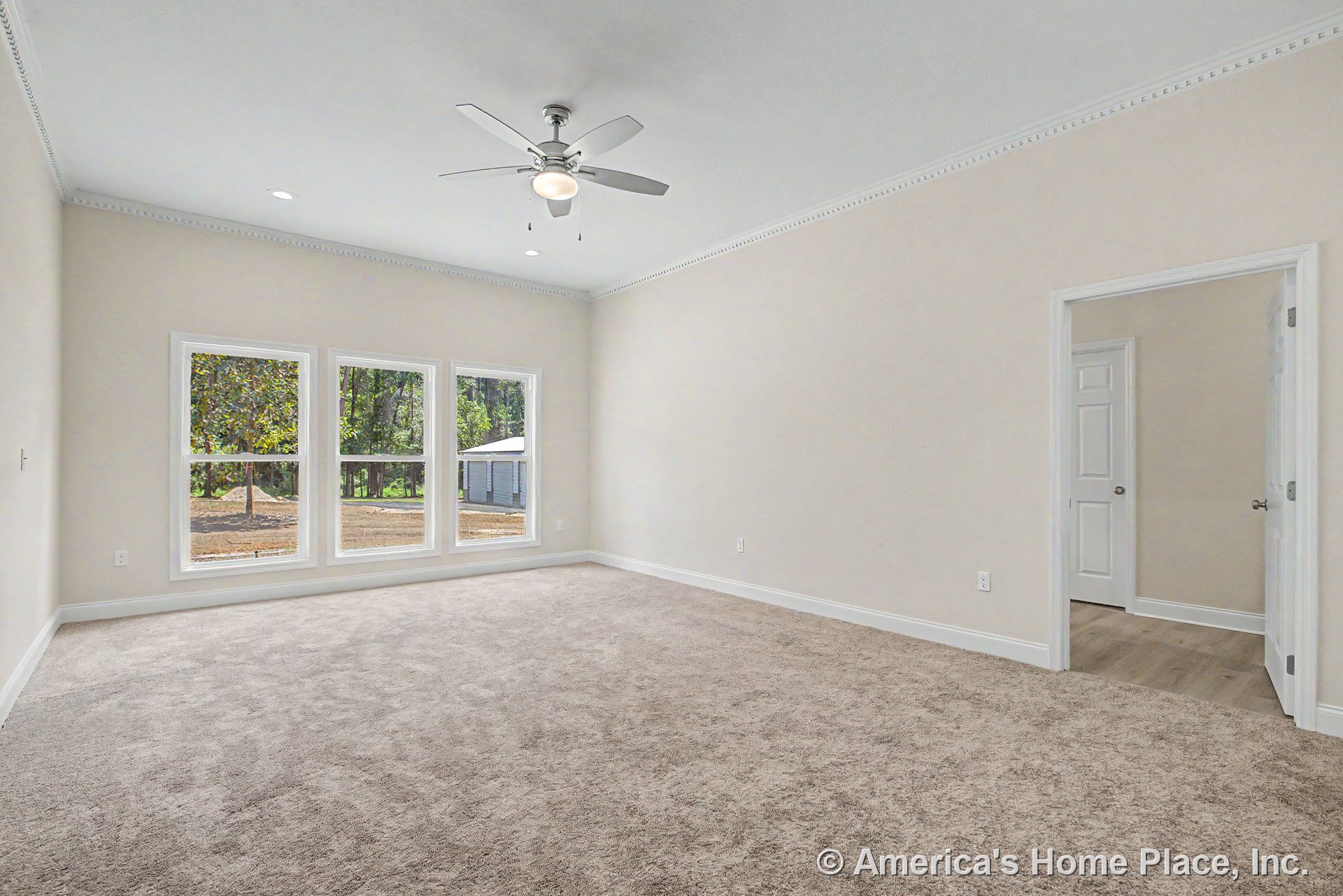 Spacious bedroom with three large windows, beige carpet flooring, ceiling fan with built-in light, white crown molding, neutral walls, white trim and baseboards, and natural light.