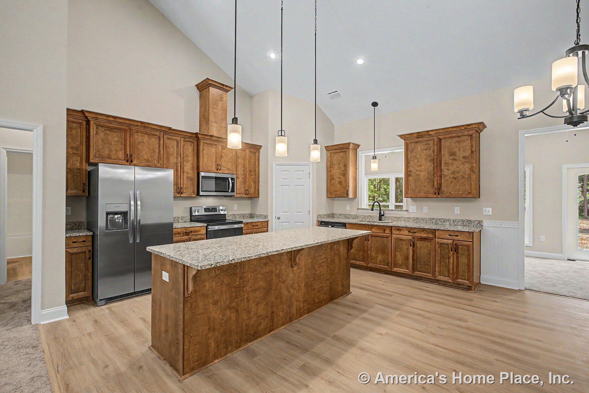 Vaulted ceiling kitchen with wood cabinetry, granite countertops, stainless steel appliances, central granite island with pendant and recessed lighting, double window above sink