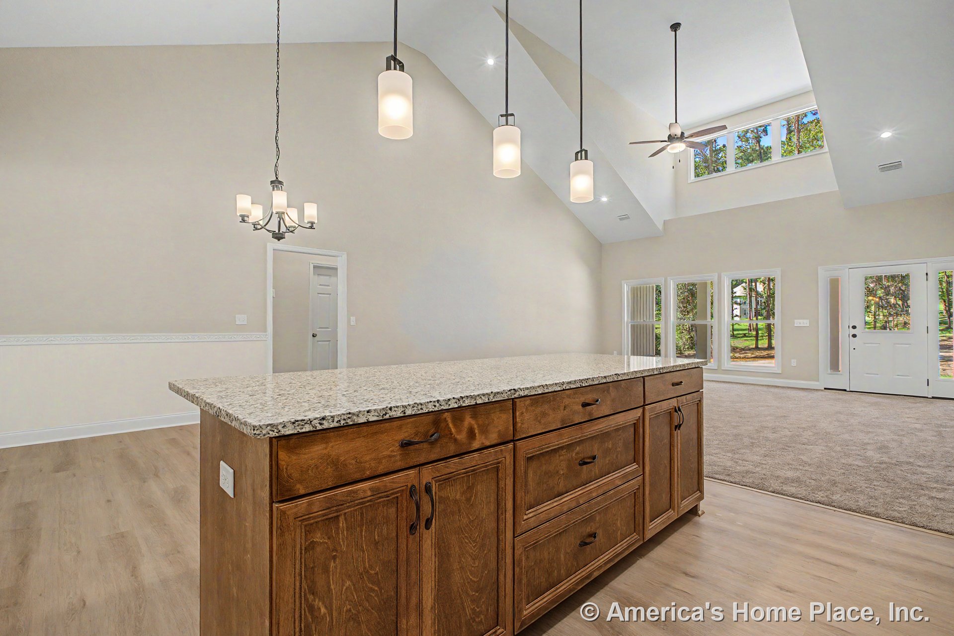 Vaulted ceiling with recessed lighting above open living area, large windows with decorative trim, kitchen island featuring granite countertop and wood cabinetry, pendant and