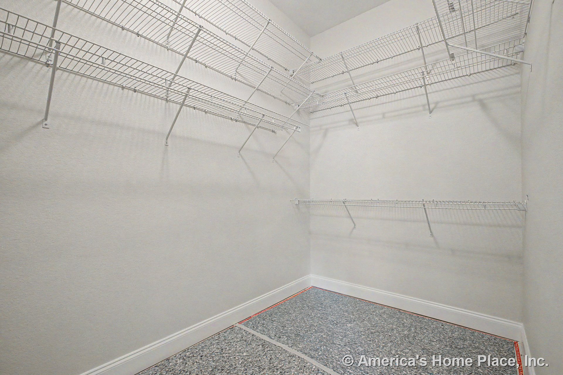 Corner walk-in closet with multiple built-in white wire shelving units, textured gray flooring, white baseboards, neutral painted walls, and a high ceiling.
