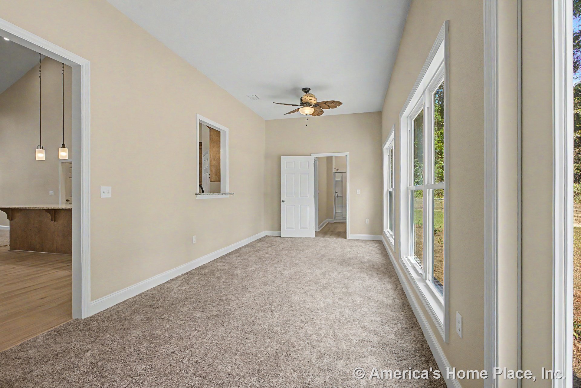 Sunroom with expansive white-trimmed windows, beige carpet flooring, leaf-shaped ceiling fan, neutral painted walls, white interior door, and pass-through window to kitchen.