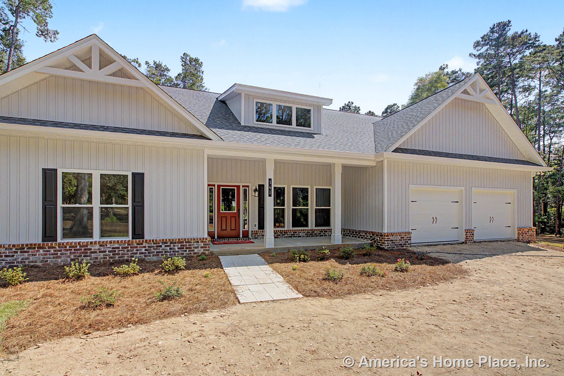 Vertical board and batten siding with brick foundation trim, covered front porch, double garage doors, front entry door with sidelights, dormer window above porch, roof gables
