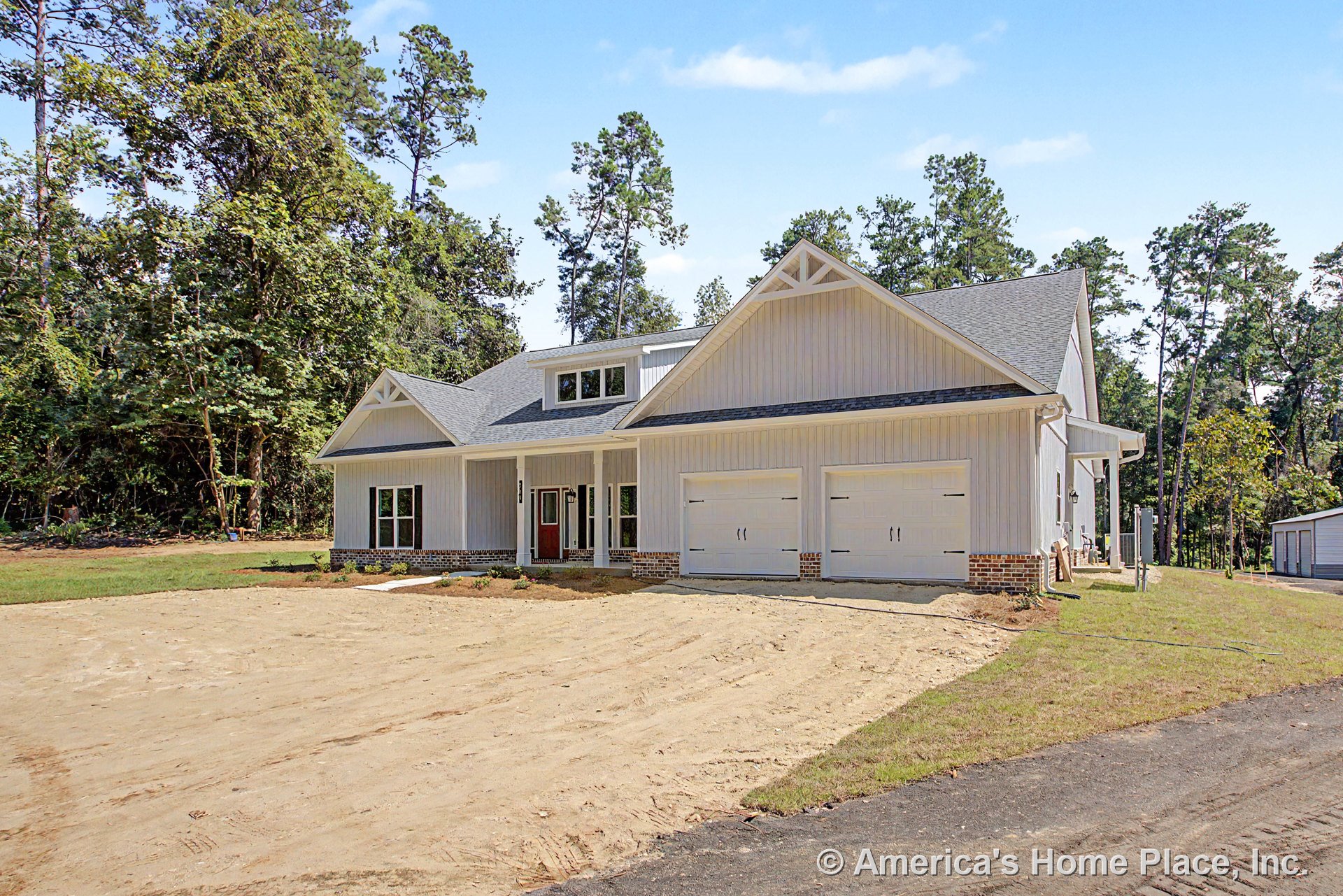 Two-car garage with white paneled doors, covered front porch, vertical board and batten siding, brick foundation trim, gable roof with decorative trusses, large front windows, and