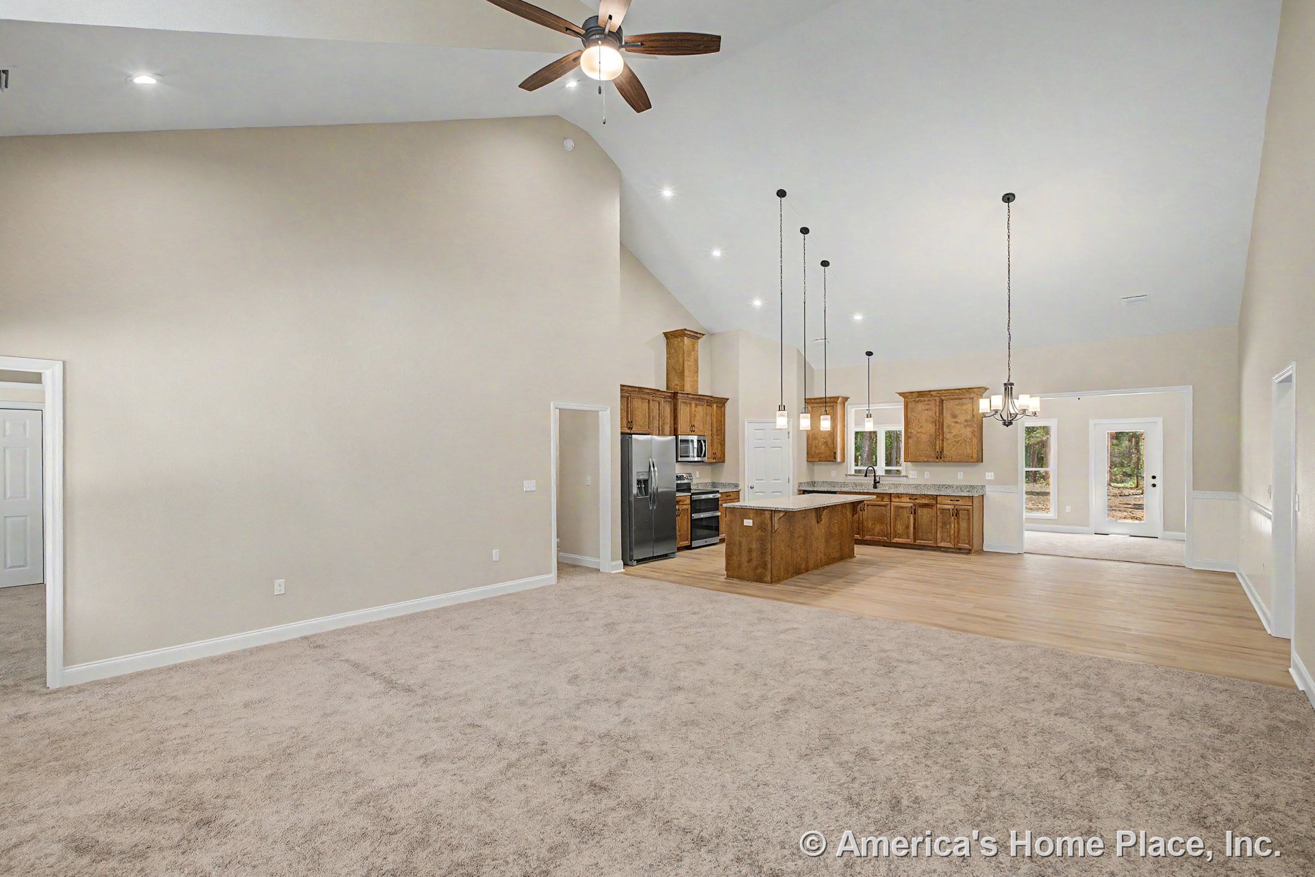 Vaulted ceiling with ceiling fan and recessed LED lighting above open living area; kitchen features wood cabinetry, granite countertops, and pendant lights over central island