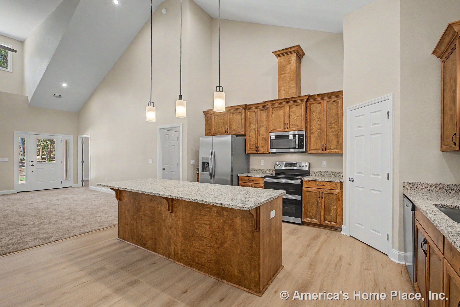 Granite kitchen island with wood upper and lower cabinets, stainless steel refrigerator, built-in microwave, vaulted ceiling featuring recessed and pendant lighting, pantry door