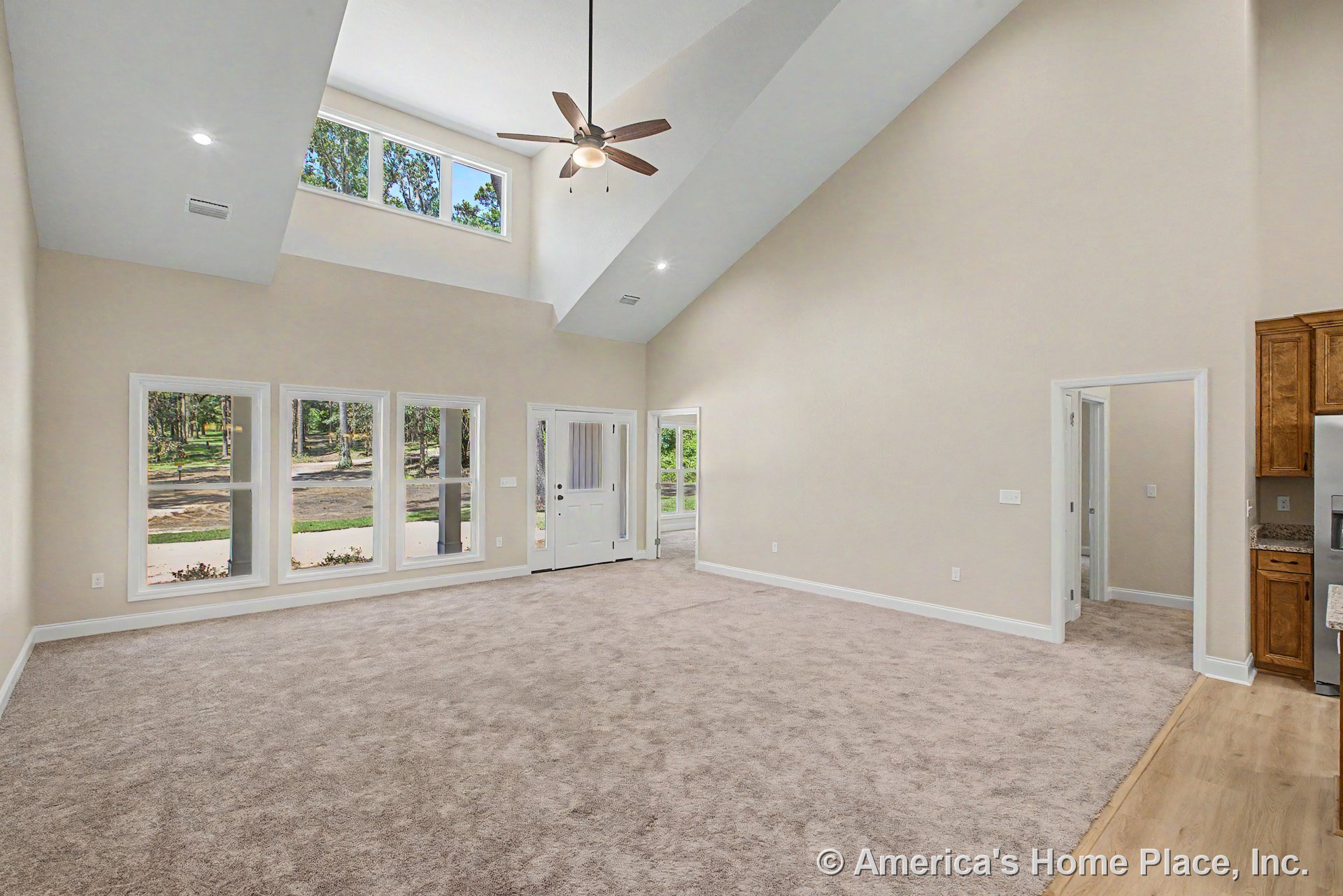 Vaulted ceiling with recessed lighting, multiple large windows along one wall, carpeted floor, white trim and baseboards, entry door featuring a glass panel, open layout connecting