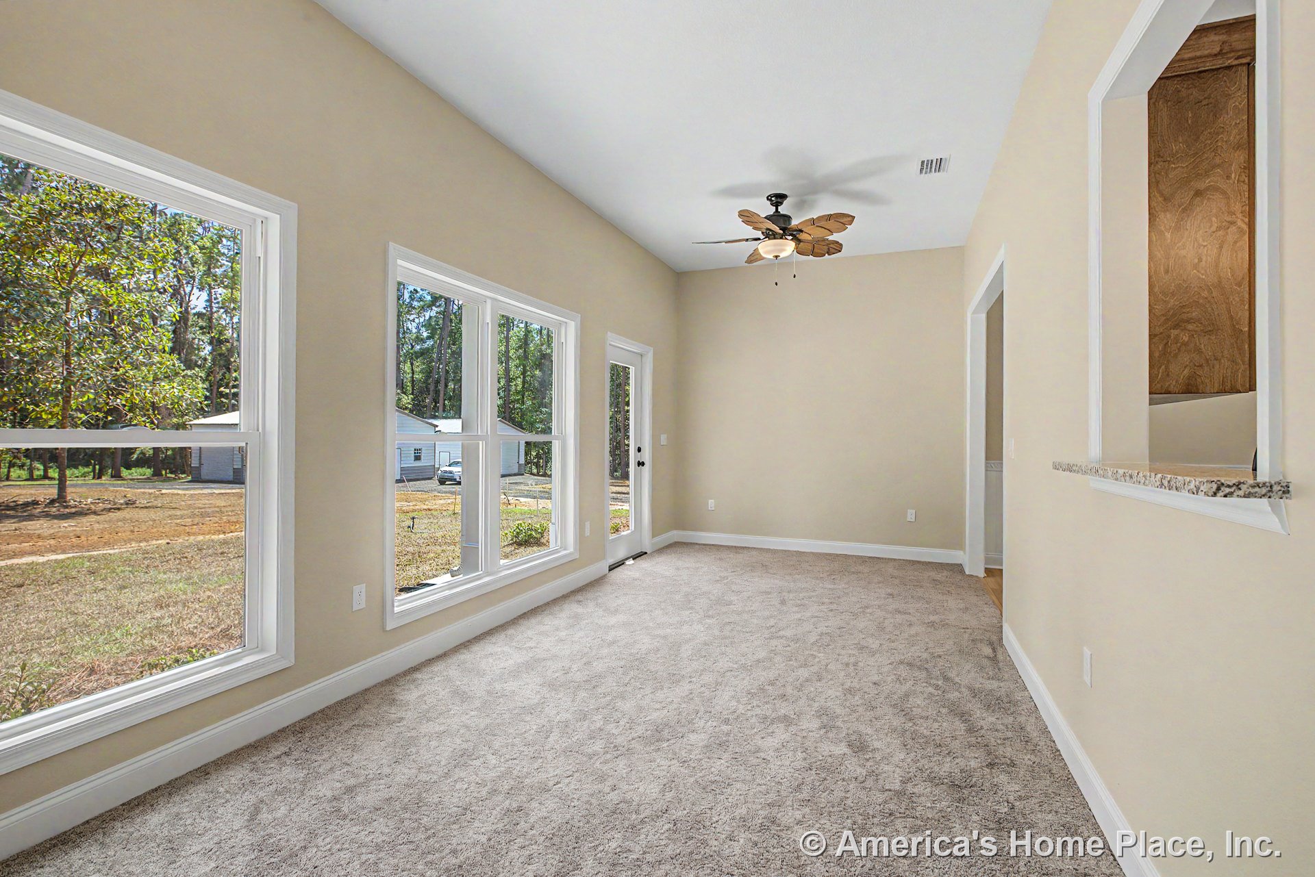 Living room with large picture windows, neutral wall paint, carpet flooring, ceiling fan with integrated light, granite pass-through ledge, white trim and baseboards, and natural