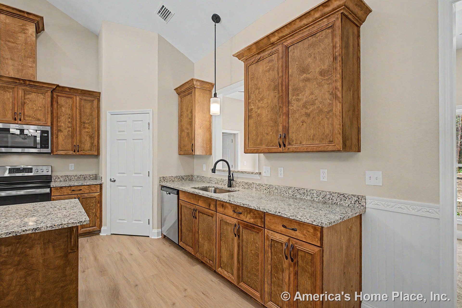 Natural wood upper and lower cabinets, granite countertops, stainless steel oven, microwave, and dishwasher, single basin sink, wood-look flooring, pendant light fixture, neutral