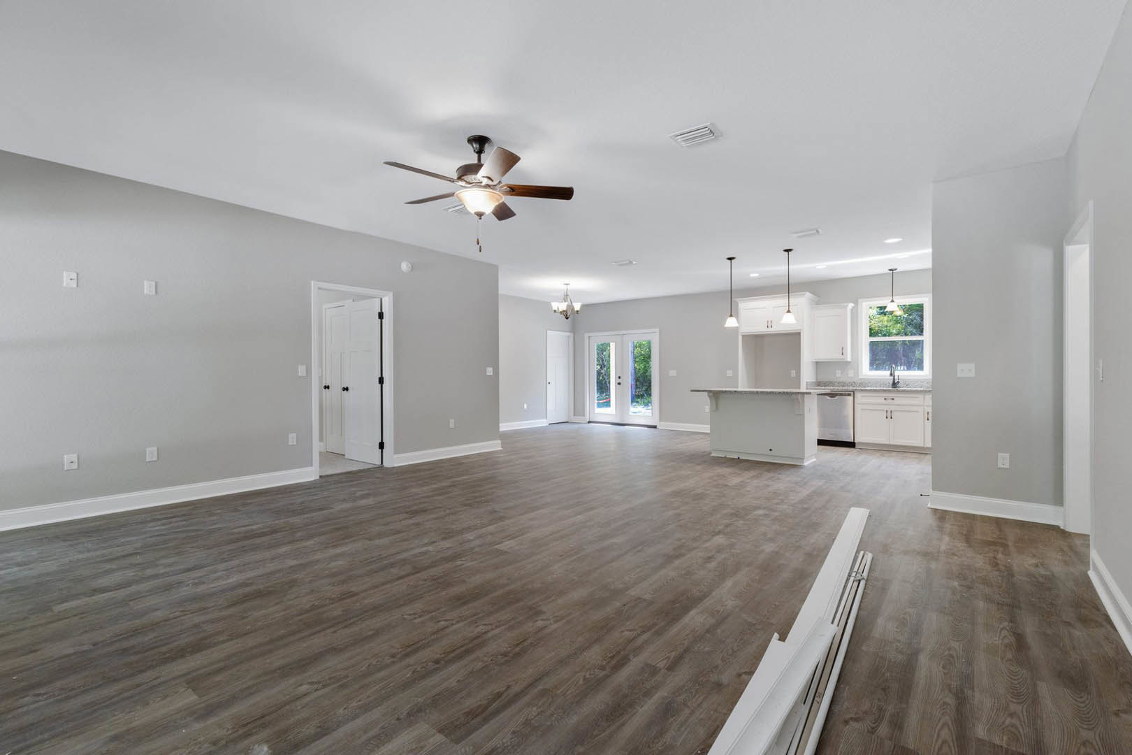 Spacious room with hardwood flooring, white walls, ceiling fan with light fixture, white door featuring black knobs and glass panels